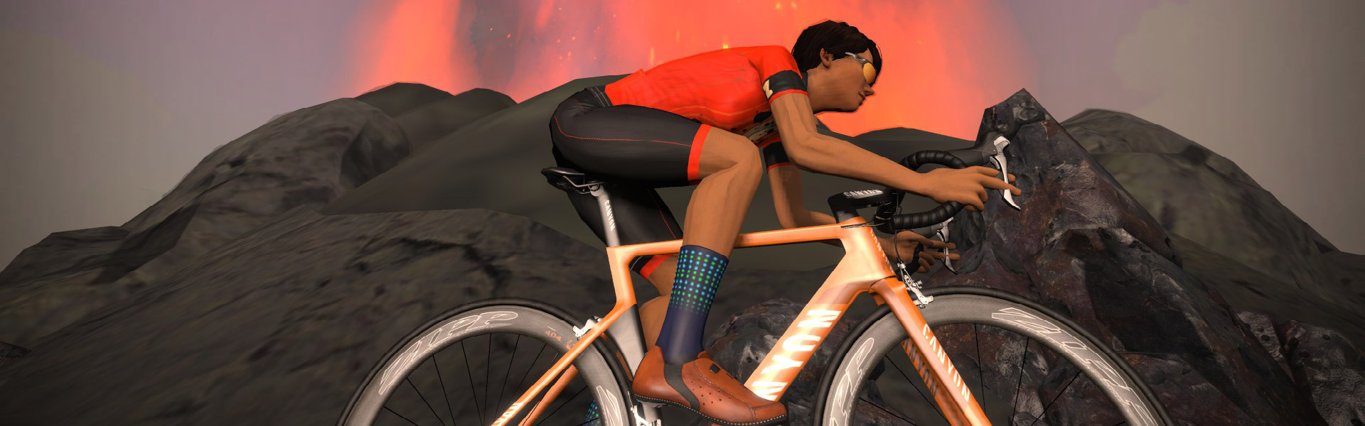A cyclist in an orange jersey and blue socks rides a road bike up a rocky incline with a volcano erupting and spewing lava in the background.