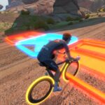 A cyclist wearing a helmet rides on a dirt road with glowing neon orange and blue tracks, surrounded by rocks and bushes, under a sunny sky.