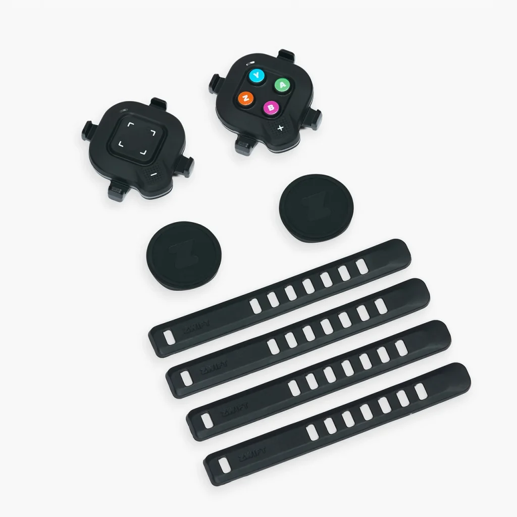 Bike computer mounts, four black rubber straps, two round covers, and a device with colored buttons are arranged on a white surface.