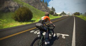 A cyclist riding a road bike on a hilly mountain road with the hashtag #GOZWIFT painted on the asphalt.