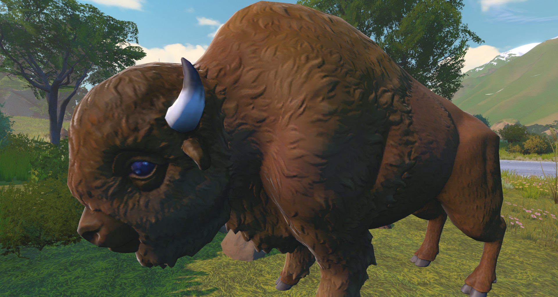 A brown American bison standing in a grassy field with trees and mountains in the background.