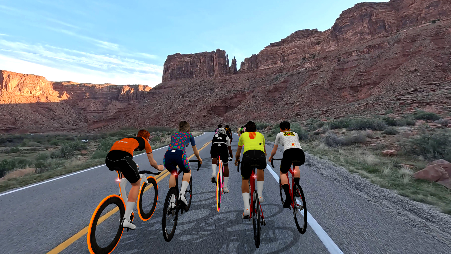 A group of cyclists riding bicycles down a desert road flanked by large rock formations.