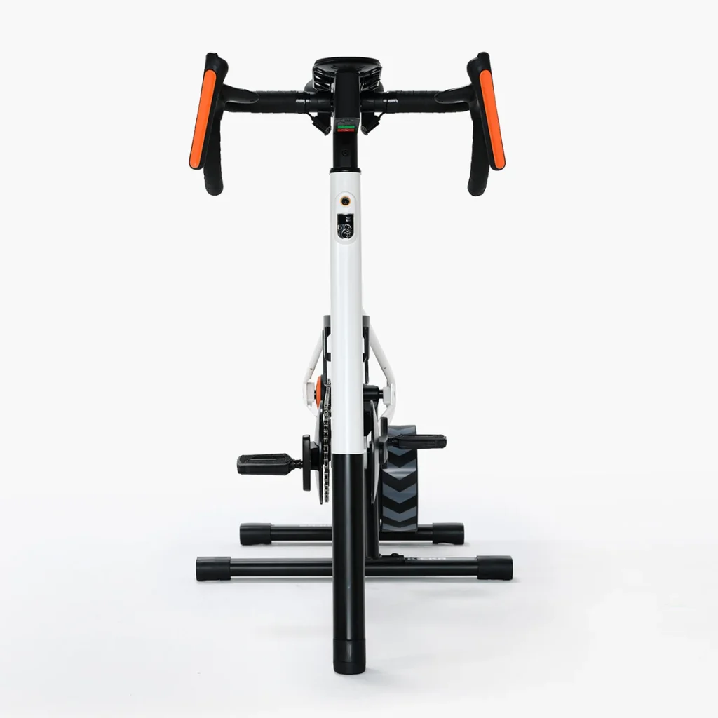 Stationary exercise bike viewed from the front, featuring a white and black frame with orange handlebar grips.